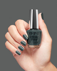 Hand with short manicured nails painted deep green holds OPI nail polish Infinite Shine bottle in shade Get in Platform-ation against a solid gray background, showcasing the glossy longwear gel-like finish for US shoppers.