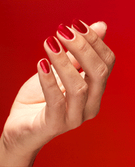 Hand tilting to showcase glossy red nails painted with Kiss My Aries OPI nail polish nail lacquer against a bold red background, highlighting the smooth, vibrant salon-quality finish for a fiery manicure look.