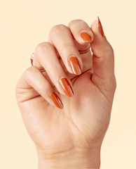 Hand with medium-length almond nails painted in OPI nail polish shade My Italian is a Little Rusty, a glossy burnt orange nail lacquer, posed against a pale beige background to showcase the warm fall color and smooth finish.