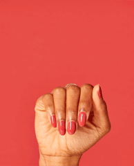 Hand showing glossy coral-red nails painted with OPI nail polish shade My Solar Clock is Ticking nail lacquer, fingers curled against a matching bold red background for a modern, salon-quality manicure look.