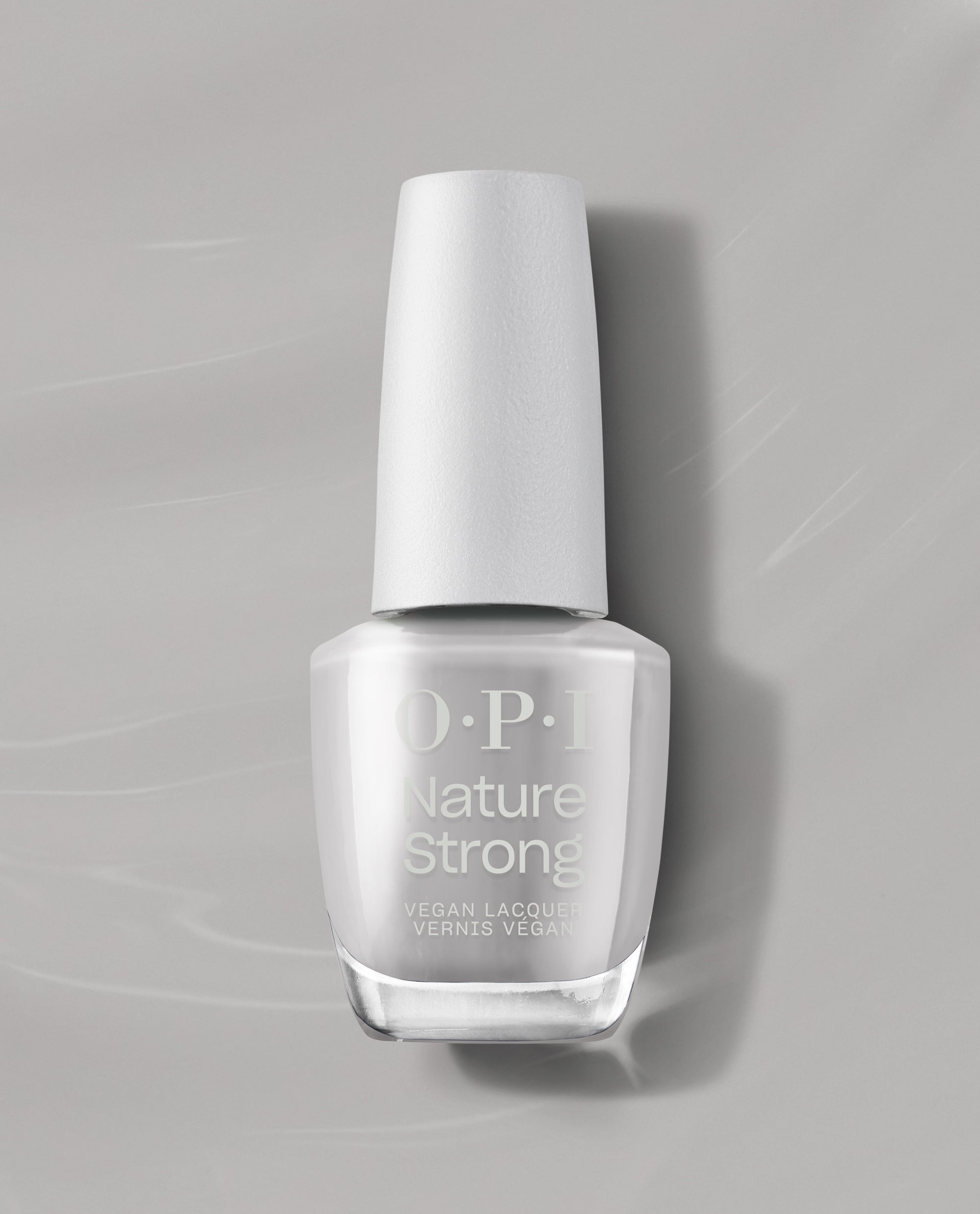 OPI Nature Strong Vegan Nail Lacquer in Dawn of a New Gray stands upright, showing a soft light gray shade in a clear bottle with a white cap on a gray background, a trending neutral nail color.