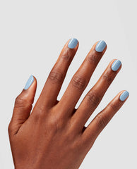 Manicured hand showcasing Baggy Jean Baby Nail Lacquer, a glossy denim-blue polish on short nails, splayed against a light gray background, highlighting a modern option for fall nail colors.