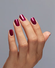 Hand with medium-length nails painted in Big Sagittarius Energy, a glossy deep magenta OPI nail polish nail lacquer, held against a plain gray background to showcase the rich color and smooth, even manicure finish.