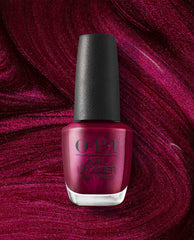 OPI nail polish bottle in the shade Big Sagittarius Energy, a deep shimmery magenta nail lacquer, standing upright against a swirling glittery berry-red background that matches the polish color.