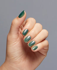 Shimmery emerald manicure showcases Feelin’ Capricorn-y Nail Lacquer by OPI, a green nail polish on short, rounded nails, hand angled to reveal glossy sparkle against a soft gray background—a fresh go-to for spring nail colors.