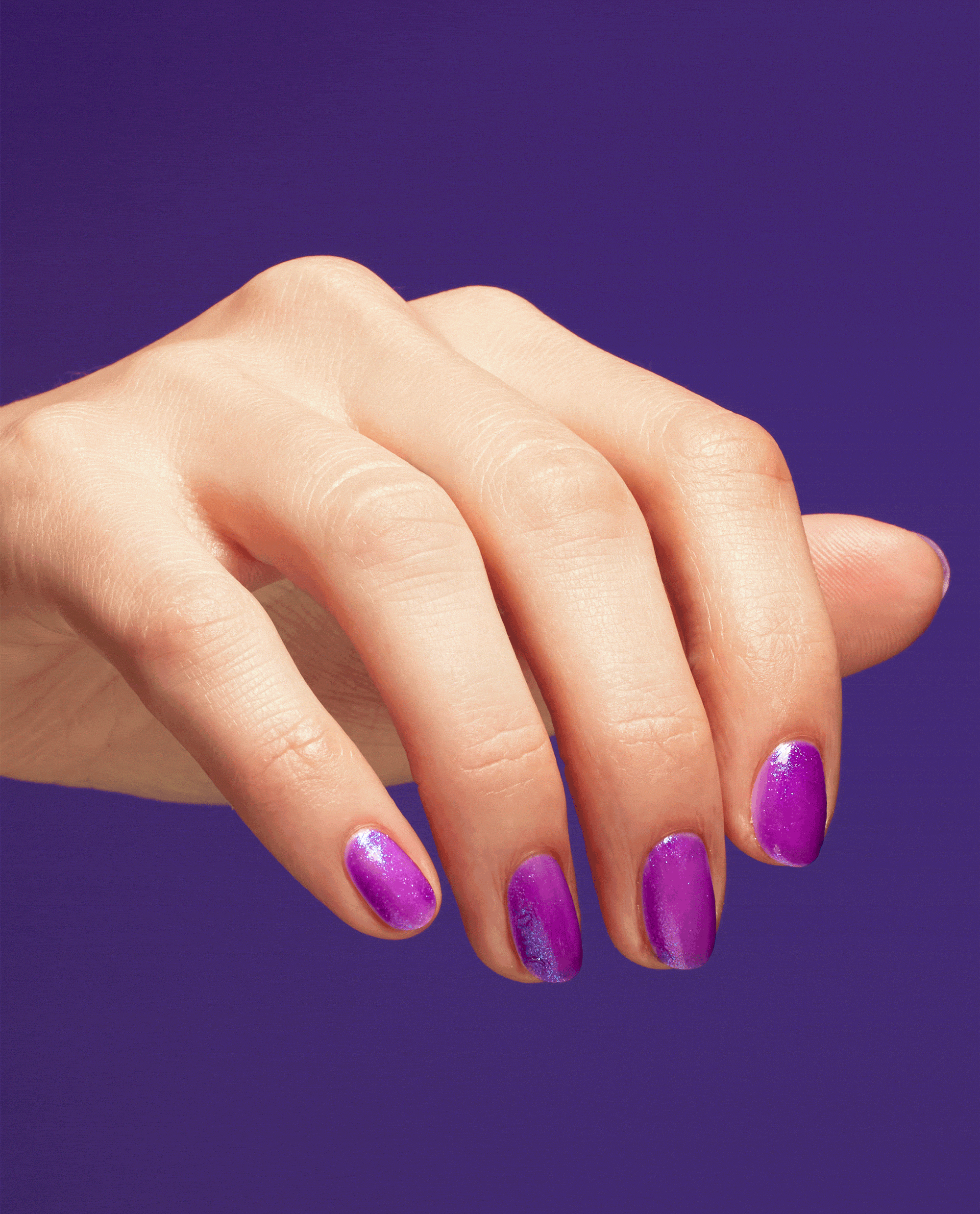 Hand with short oval nails wearing Feelin’ Libra-ted OPI nail polish, a vibrant shimmery purple nail lacquer, resting against a solid purple background to showcase the bold zodiac-inspired manicure color.