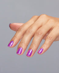 Hand displaying short, neatly manicured nails painted with Feelin’ Libra-ted, a bright shimmery purple OPI nail polish, against a plain gray background, showcasing the glossy, iridescent nail lacquer finish.