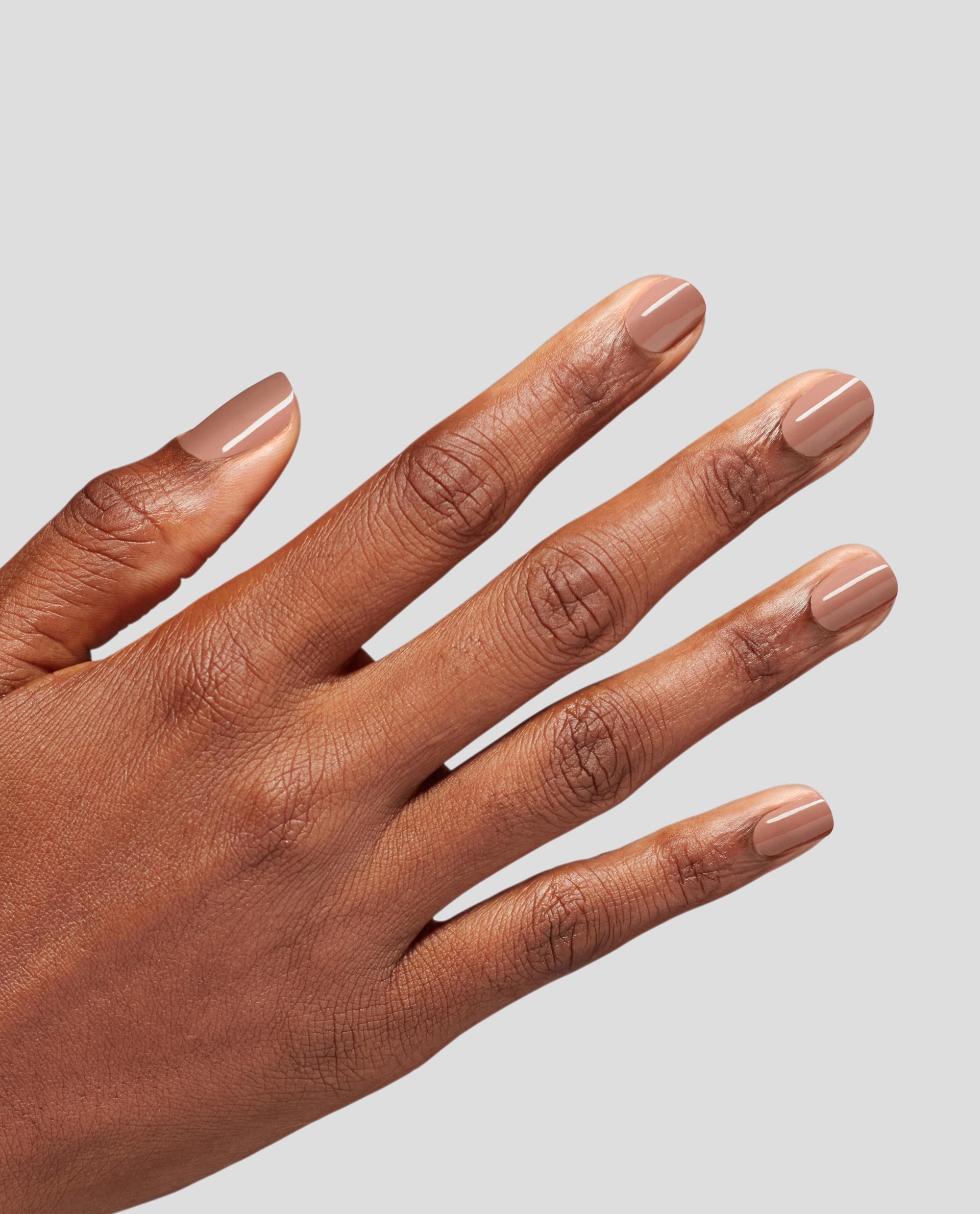 Hand with short, neatly manicured nails painted in Flannel Aerobics, a creamy beige OPI nail polish nail lacquer, shown against a light gray background to highlight the smooth, glossy neutral finish for everyday wear.