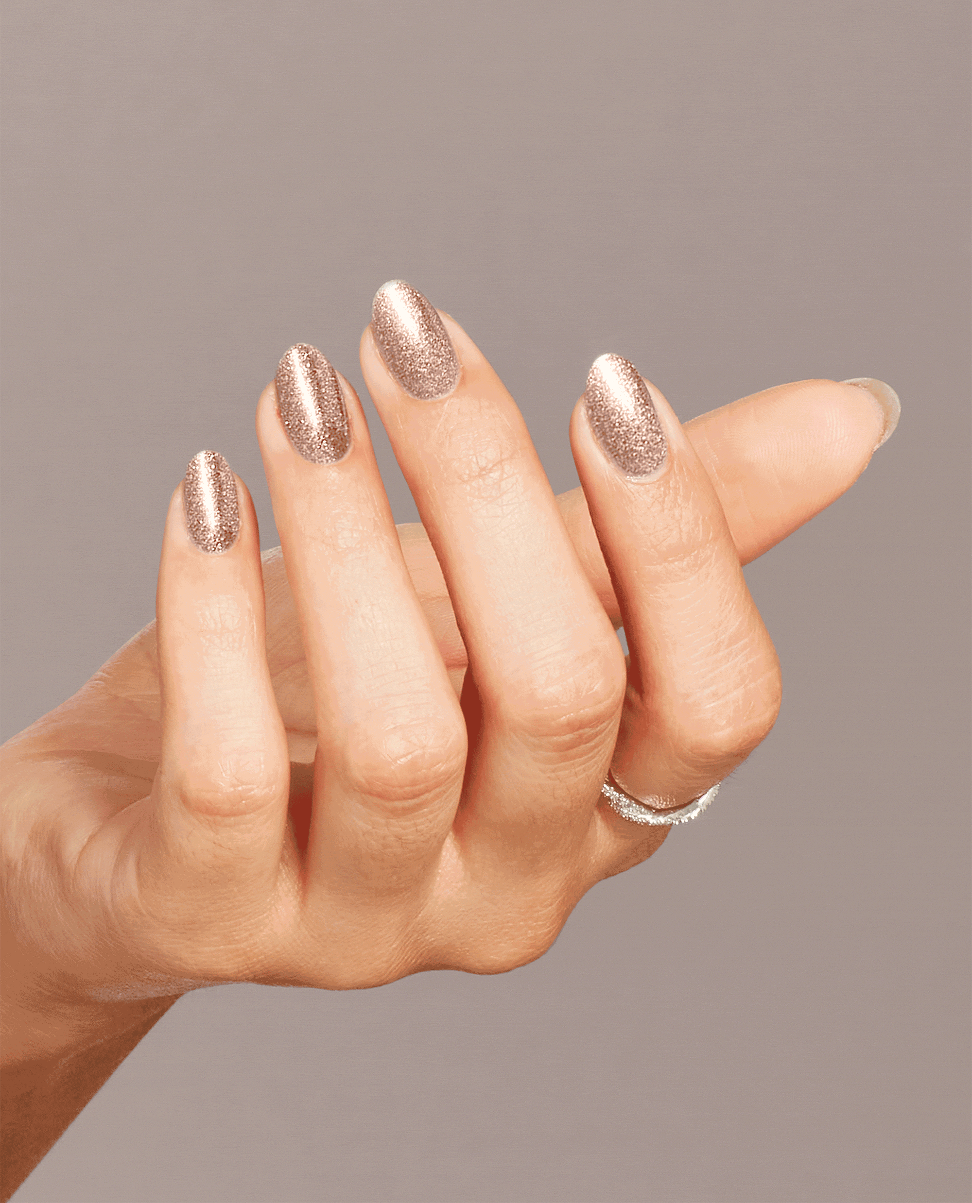 Hand models shimmering rose-gold Metallic Composition nail lacquer, showing off glossy glitter OPI nail polish on neatly shaped nails against a soft taupe background.