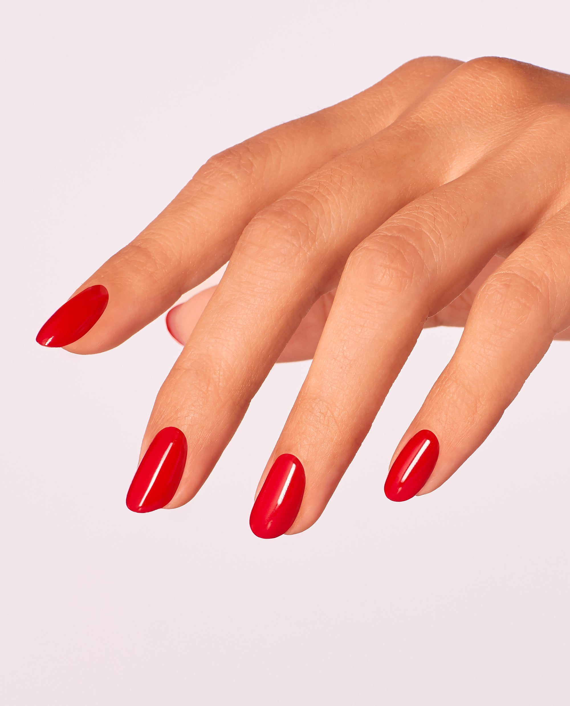 Hand with neatly manicured oval nails showcases Red Heads Ahead OPI nail polish, a glossy bright red nail lacquer, against a clean light pink background, highlighting the vibrant color and smooth, even coverage for salon-quality nails at home.