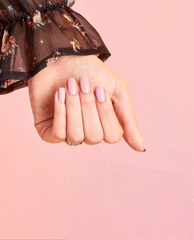 Hand with neatly manicured nails painted in Seven Wonders of OPI nail lacquer, a soft pastel pink OPI nail polish, posed against a peach-pink gradient background with a sheer floral sleeve for a chic, feminine look.