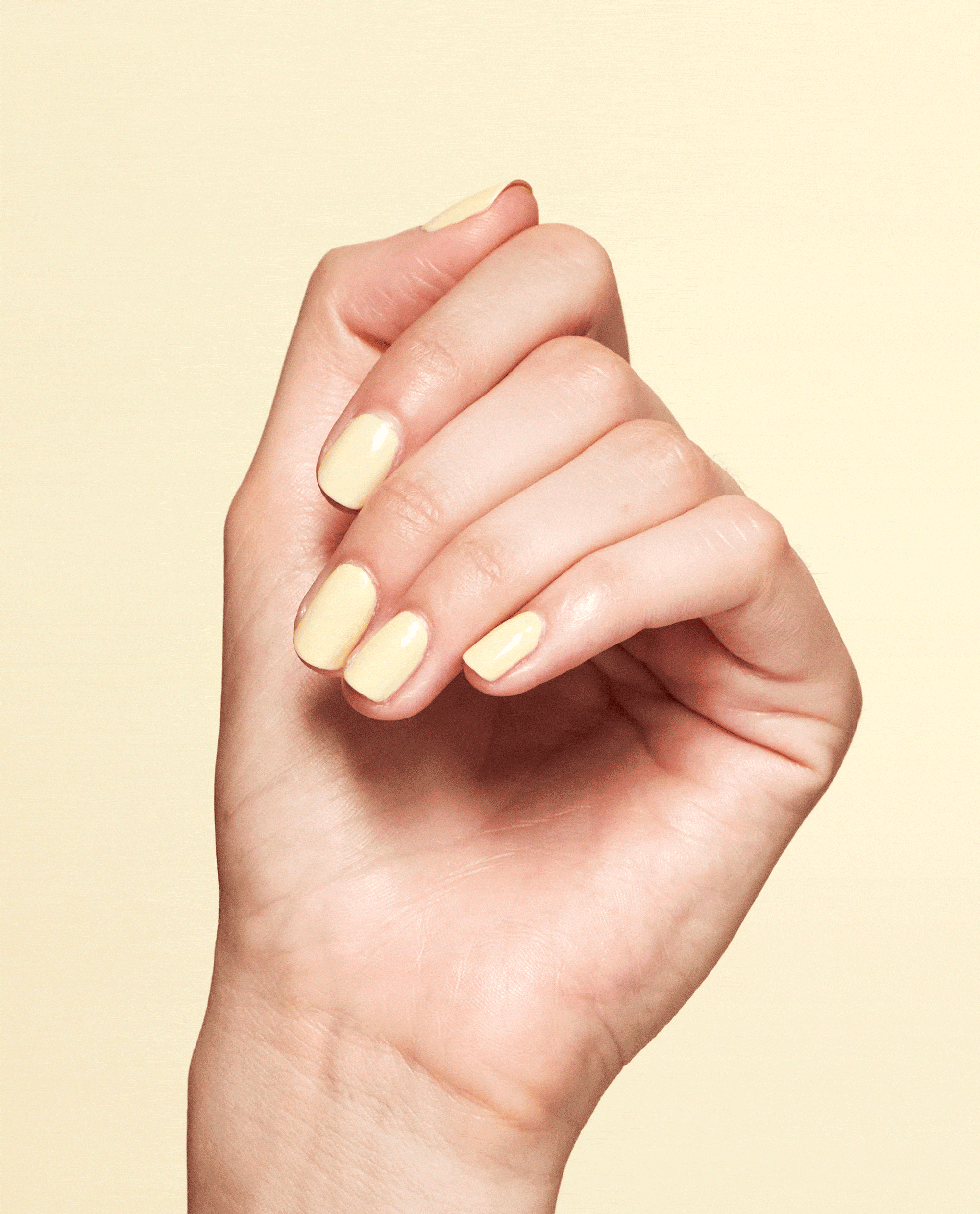 Hand with glossy pale yellow nails showcasing OPI Blinded by the Ring Light Nail Lacquer against a soft yellow background.