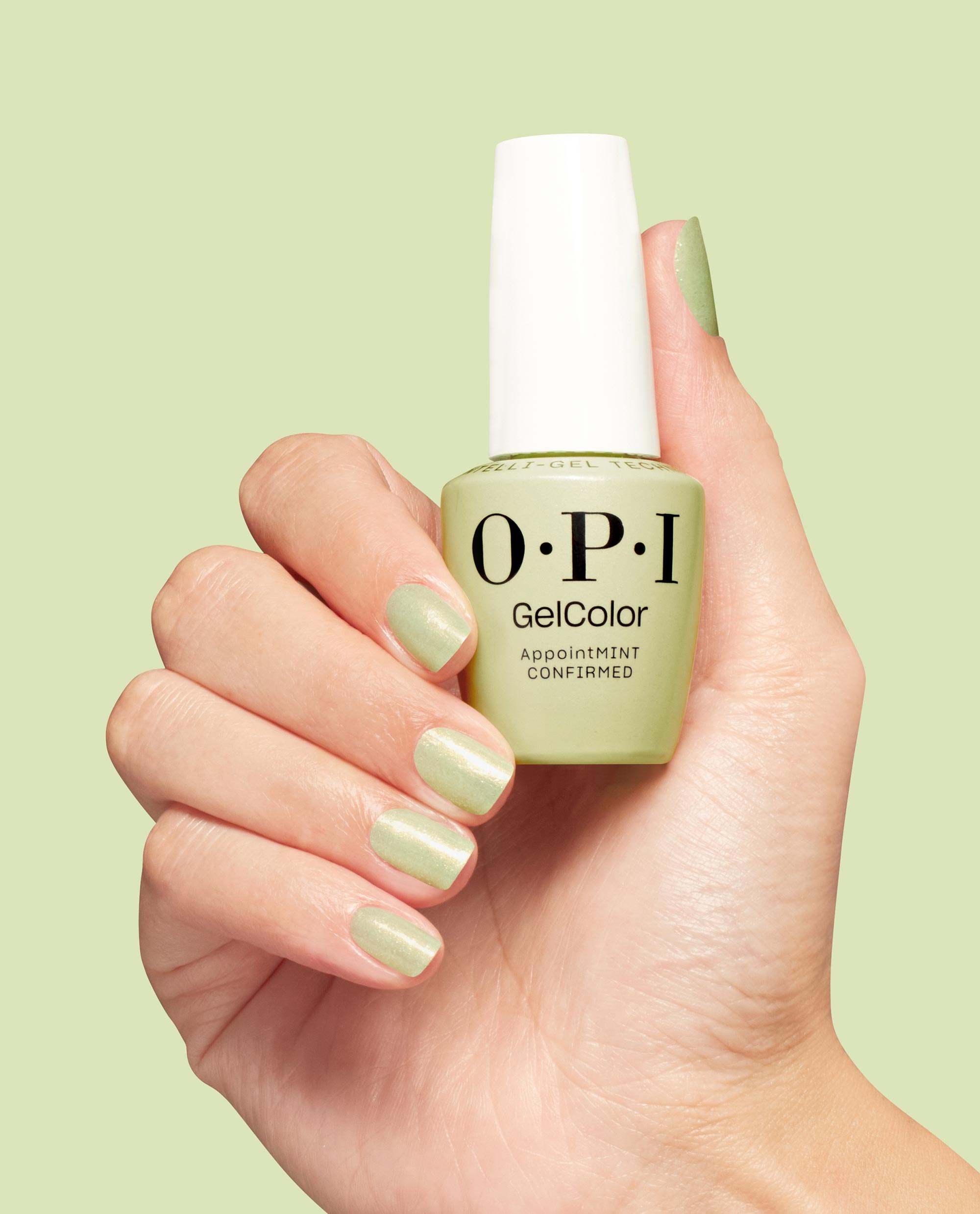 OPI GelColor AppointMINT Confirmed bottle held by a hand with matching shimmery mint manicure, showcasing green nail polish ideal for spring nail colors; gel nail polish with white cap on a light green background.