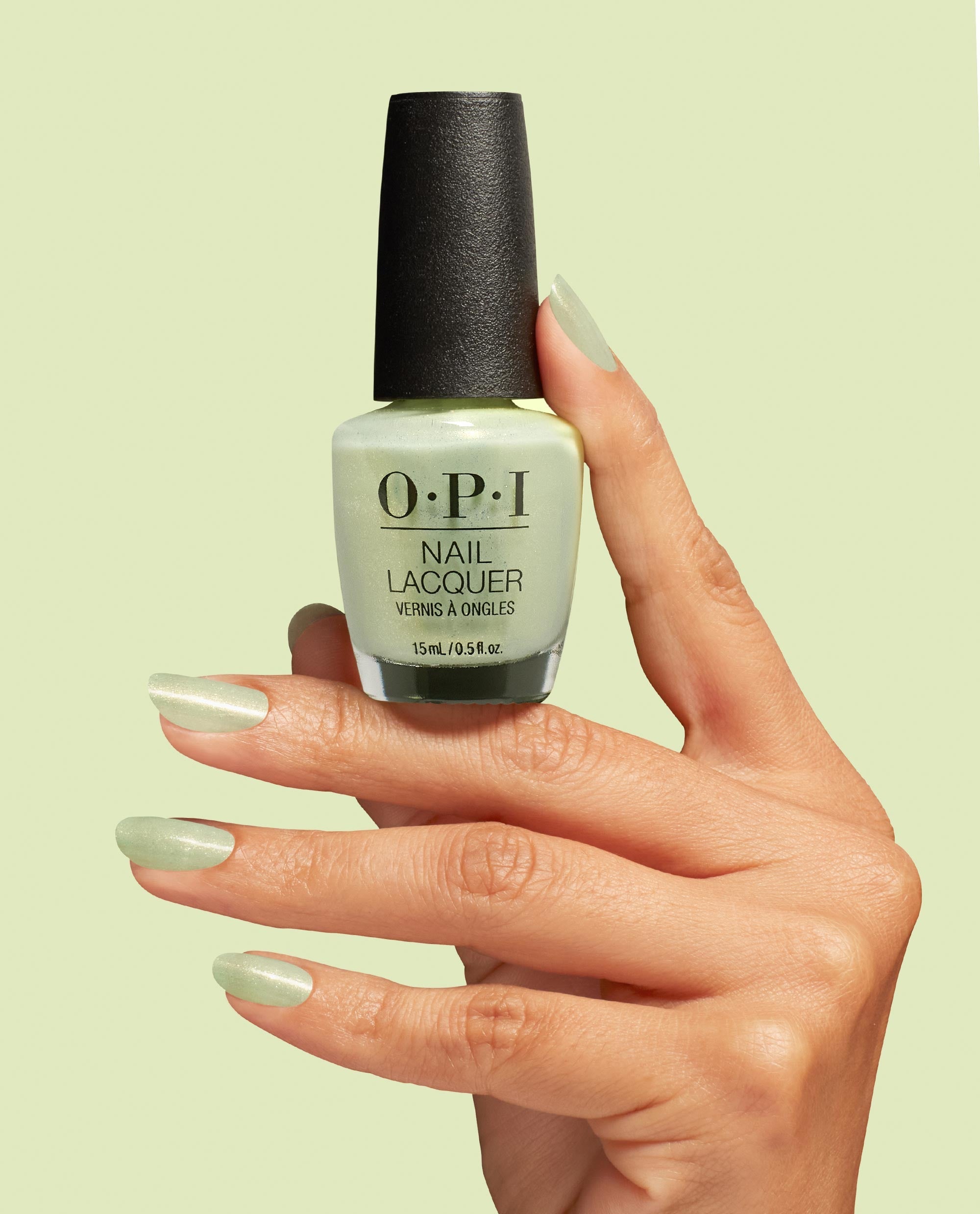 OPI AppointMINT Confirmed nail lacquer bottle held by a manicured hand with matching shimmery mint nails against a pale green background, showcasing green nail polish perfect for spring nail colors from OPI, 15 mL/0.5 fl oz.