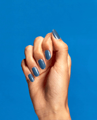 Hand with neatly manicured nails showcases Suzi Takes a Sound Bath OPI nail polish, a glossy muted blue nail lacquer, against a solid bright blue background for a modern, minimalist beauty product closeup.
