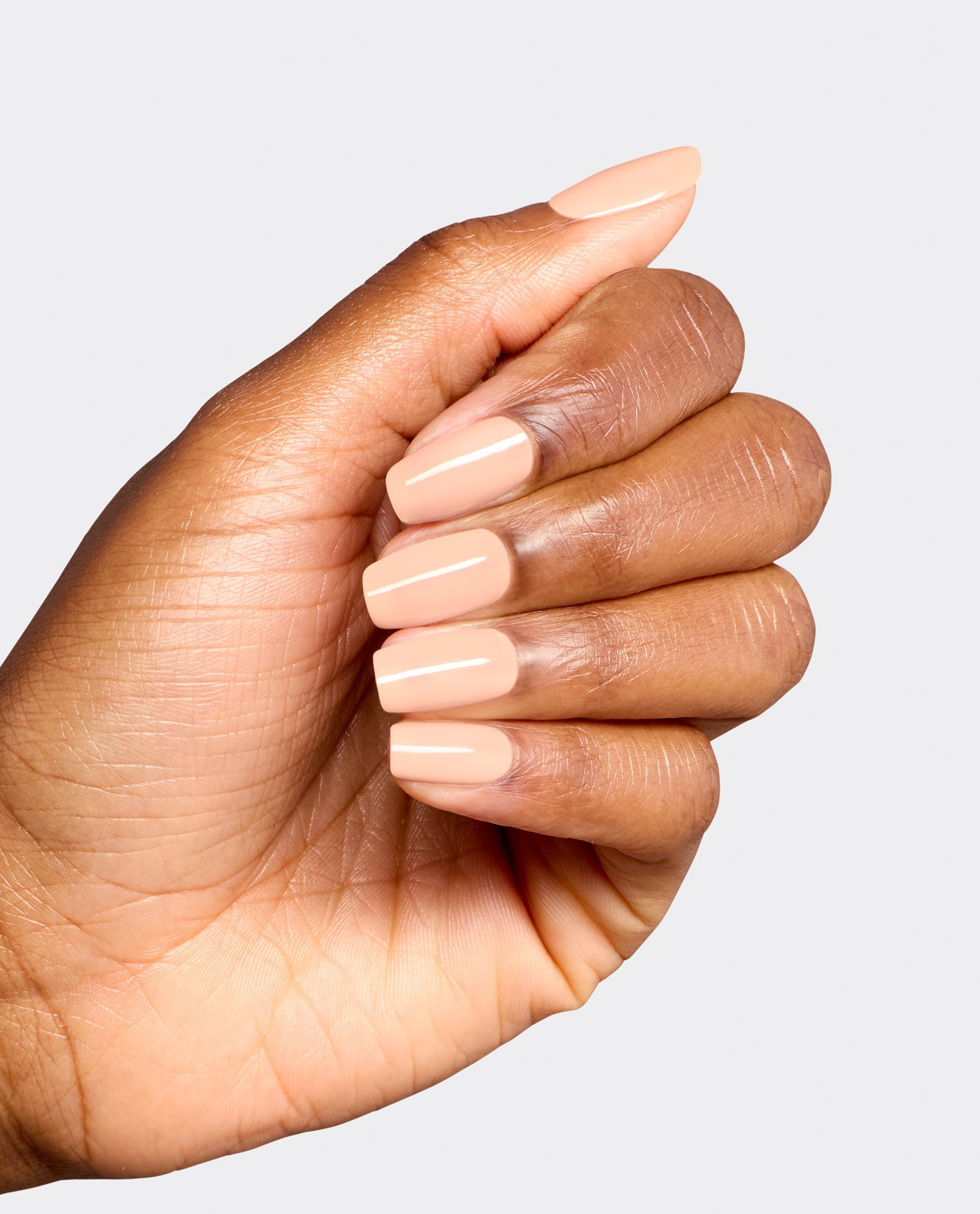 Hand displays glossy peach-nude OPI Suzi Take a Vow Gel Nail Polish on squared nails, a soft neutral shade for fall nail colors against a light gray background.